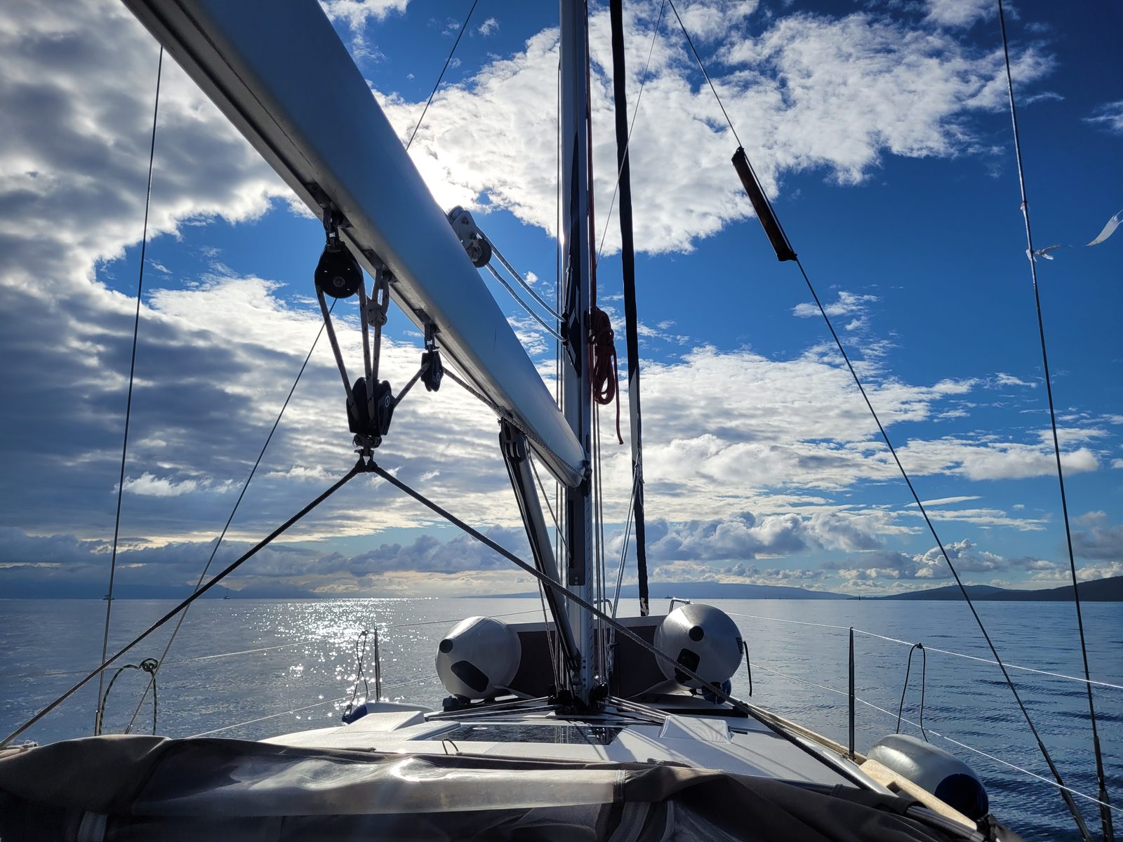 View forward along Sileb's deck under way — mast, boom and calm, sunlit sea on a flat-calm morning.