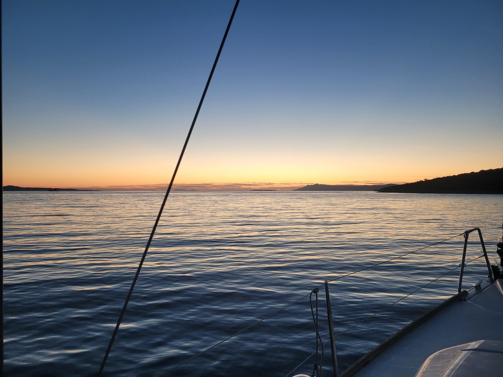 A calm golden sunset over glassy water, seen from the boat's guardrail off Pelješac.