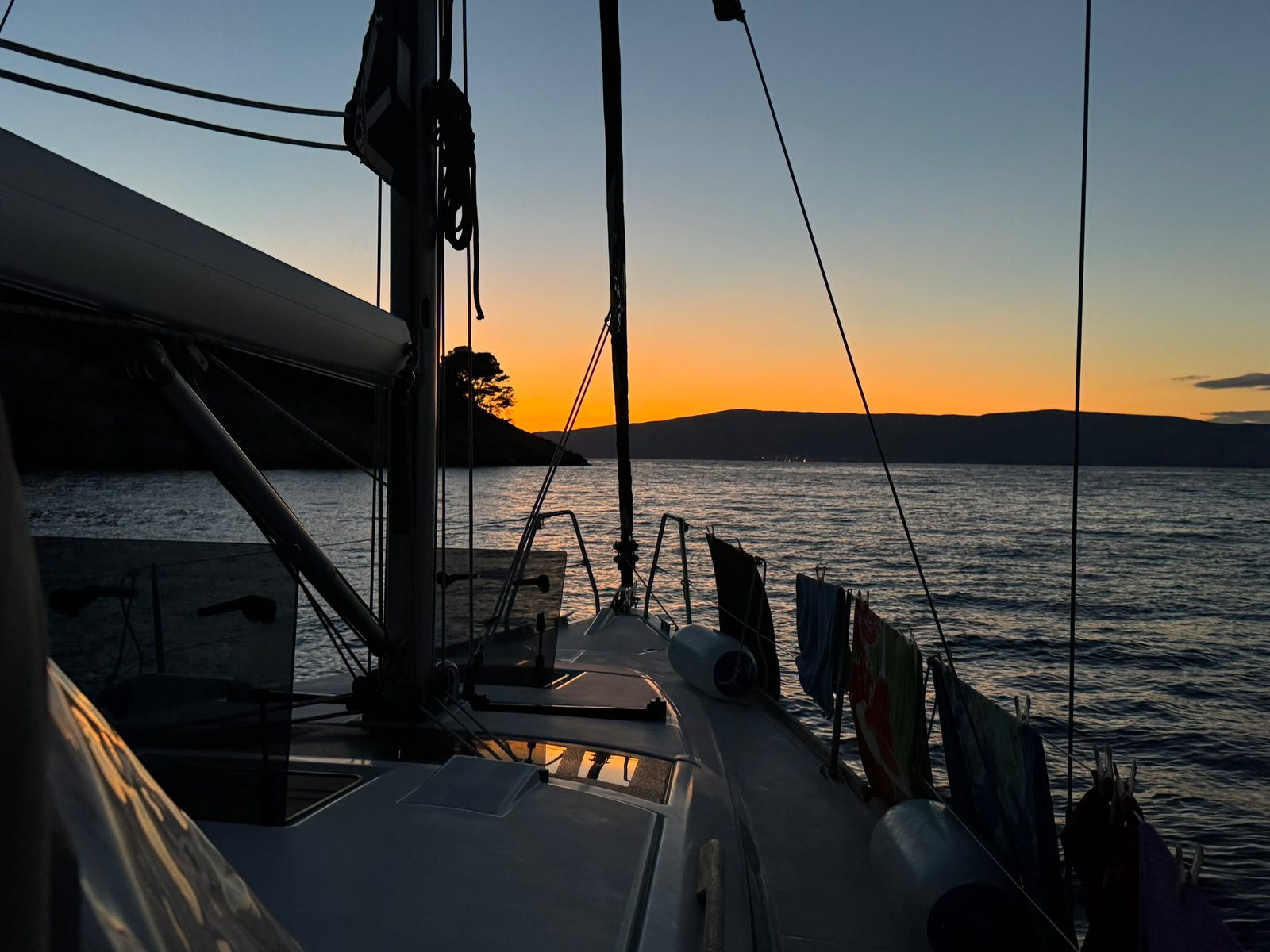 Dusk from the anchored boat, towels drying on the guardrail, an orange sky fading over the hills.